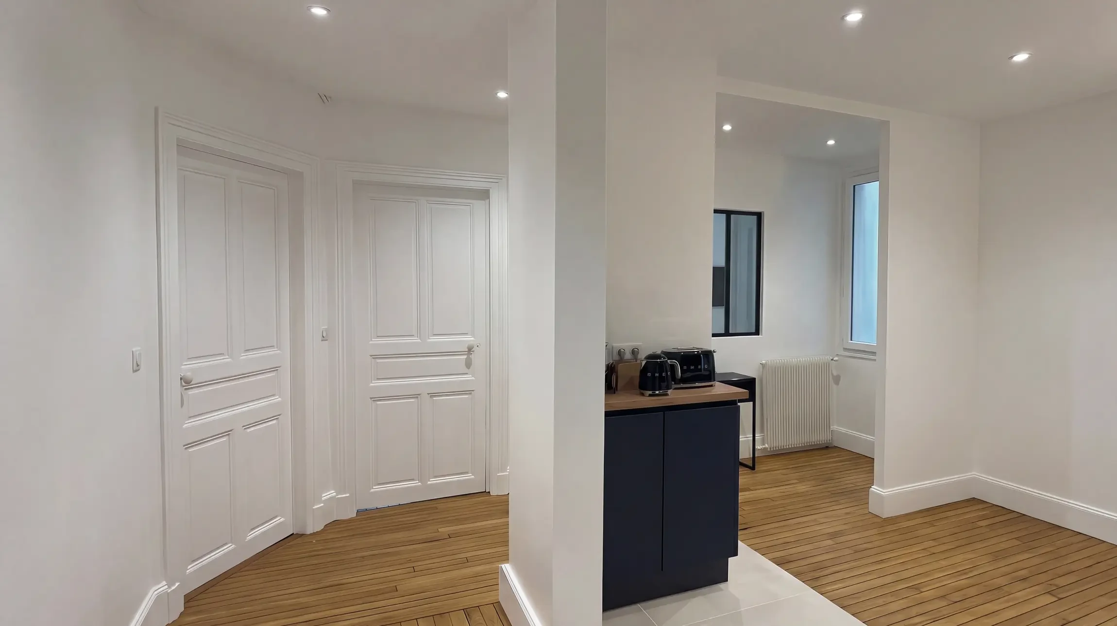 Intérieur résidentiel moderne avec couloir et trois portes en bois ouvertes donnant accès à différentes pièces : salle de bain carrelée, chambre et salon lumineux